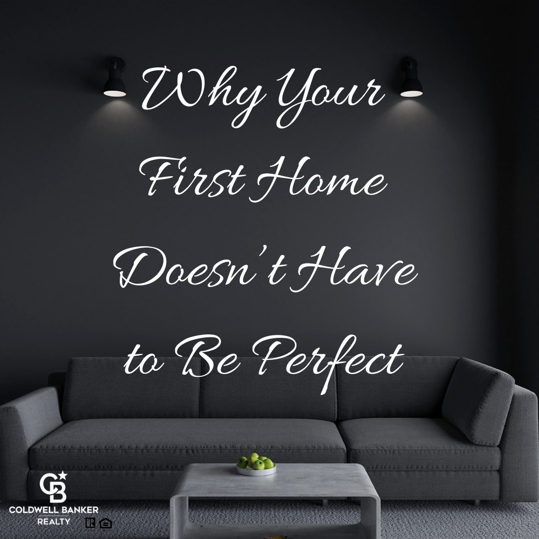 Modern living room with dark walls, black sofa, and a coffee table with green apples. White script text on the wall reads: ‘Why Your First Home Doesn’t Have to Be Perfect.’ Coldwell Banker Realty logo displayed in the corner
