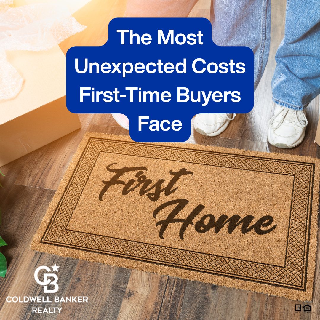 Doormat reading “First Home” on hardwood floor beside moving boxes and two people’s sneakers, with a blue overlay that says “The Most Unexpected Costs First-Time Buyers Face.”
